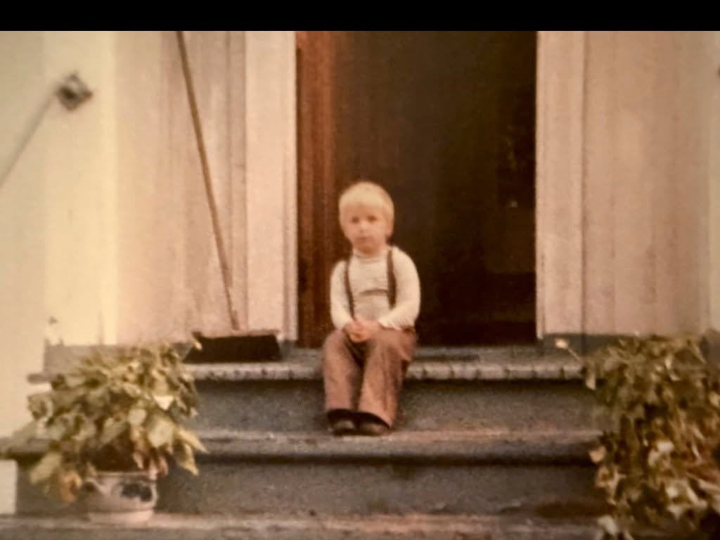 Simon Stranger as a young boy, sitting on the steps outside his home